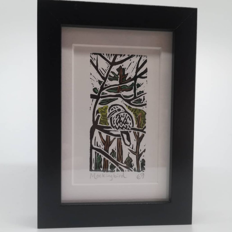 A framed linocut print of a mocking bird surrounded by trees.