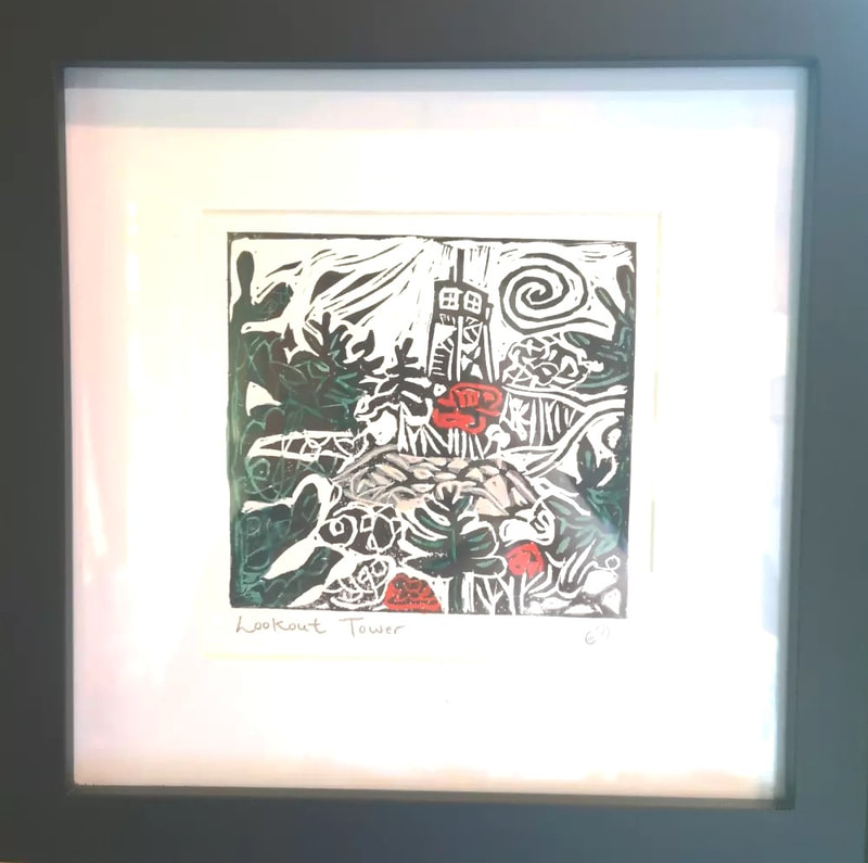 A framed square linocut print featuring a lookout tower in the distance and hills, green trees and red flowers in the foreground.