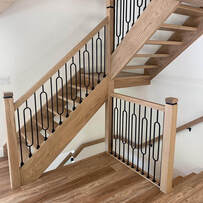 Modern wooden staircase with decorative black balusters in a white home with wood floors