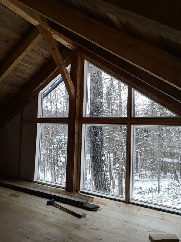 View from the upstairs of a timber frame structure looking out on a wintery forest.