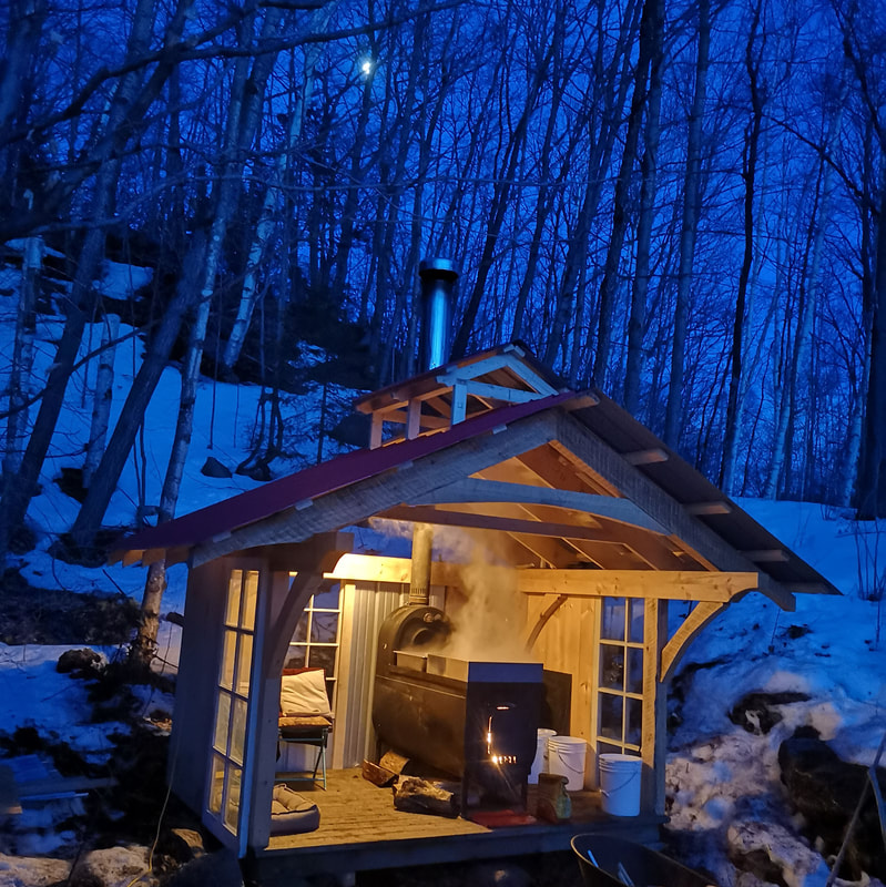 A warm, cozy timber frame sugar shack sitting in a dark, snowy forest.