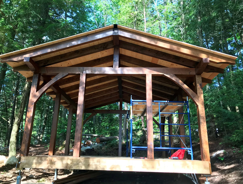 TImber frame structure in progress located in a forested area.